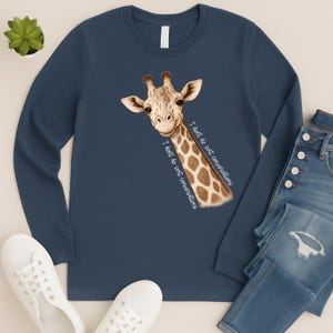 May include: A navy blue long-sleeved top with a giraffe graphic and the text "I don't do soft conversations." The giraffe has a brown and white pattern. The image also shows blue jeans and white trainers.