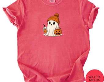 May include: A red t-shirt featuring a cartoon ghost wearing an orange beanie and holding a pumpkin-shaped candy bucket and a drink. The ghost has a friendly expression. The shirt is a solid color and has a round neckline.