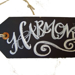 May include: A black chalkboard tag with a white string and a brown button. The tag has the word "Harmony" written in white cursive lettering with a white swirl design.