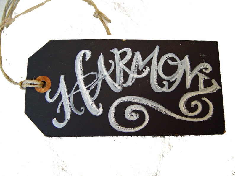 May include: A black chalkboard tag with a white string and a brown button. The tag has the word "Harmony" written in white cursive lettering with a white swirl design.