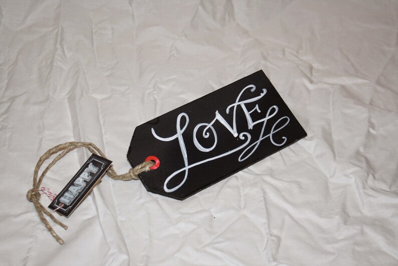 May include: Black tag with a white handwritten word "LOVE" on it. The tag is attached to a twine string with a smaller tag that says "HAPPY" on it.