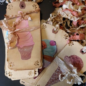 May include: A stack of brown paper gift tags with a scalloped edge. Each tag features a different ice cream cone design with the words "ICE CREAM" printed on one tag. The tags are tied with white and brown ribbon.