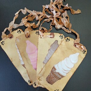 May include: Five vintage-style paper tags with a scalloped edge, each featuring a hand-painted ice cream cone in a different color. The tags are tied together with brown ribbon and have the words "ICE CREAM" printed on one of the tags.