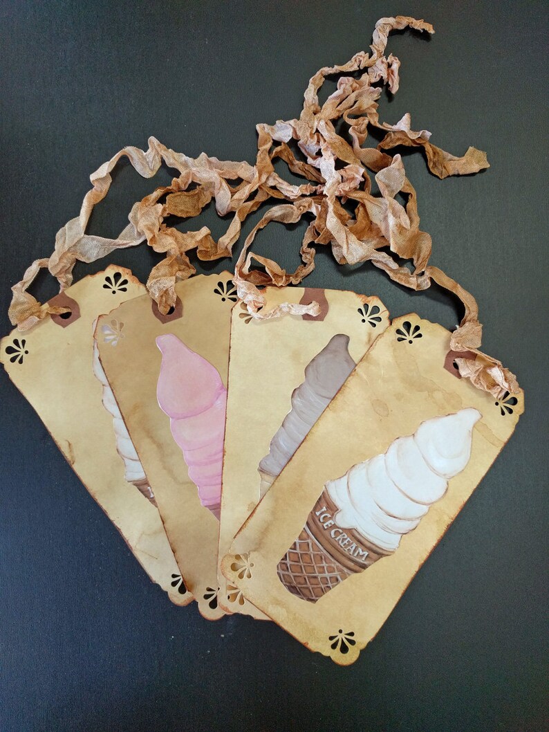May include: Five vintage-style paper tags with a scalloped edge, each featuring a hand-painted ice cream cone in a different color. The tags are tied together with brown ribbon and have the words "ICE CREAM" printed on one of the tags.