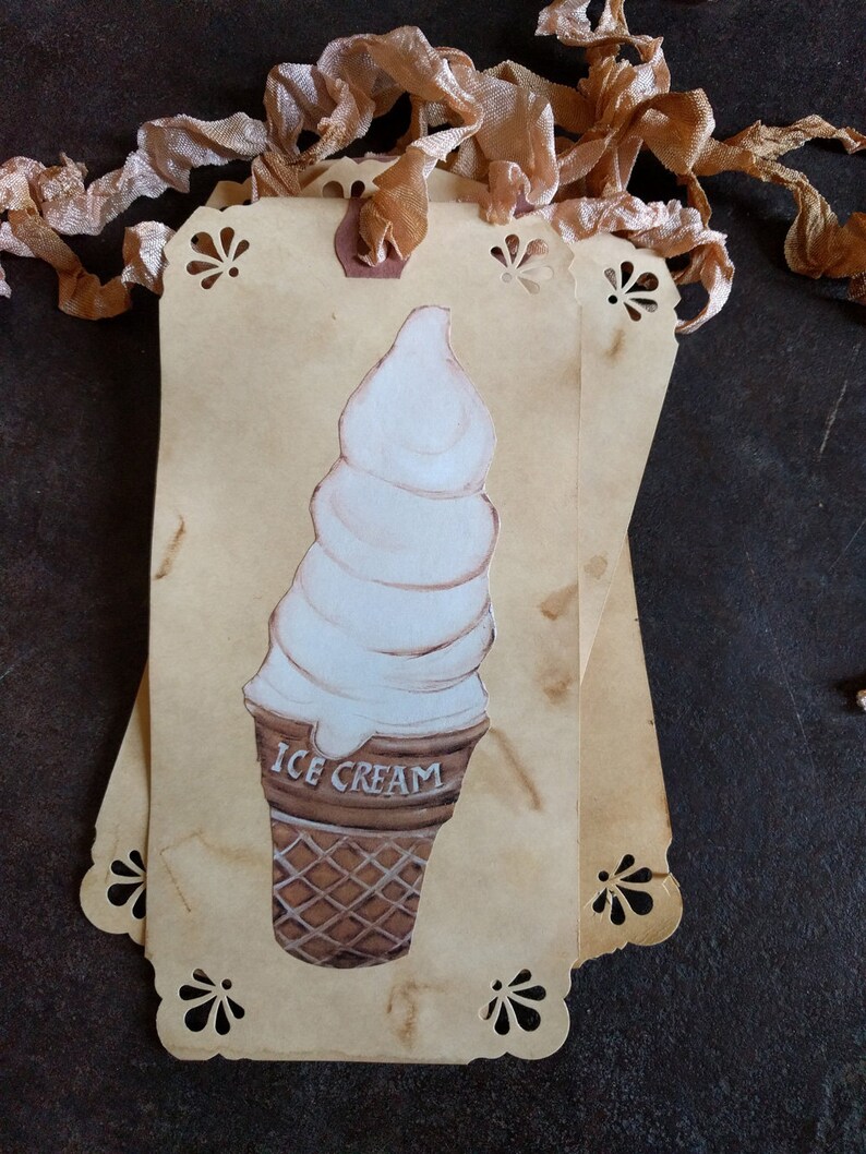 May include: A vintage-style tag with a hand-painted illustration of a white ice cream cone on a brown background. The tag has a scalloped edge and the words "ICE CREAM" are printed on the cone.