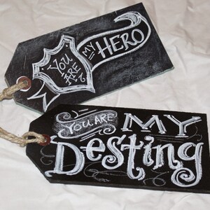 May include: Two black chalkboard tags with white chalk lettering. The top tag says "You are my hero" with a banner design. The bottom tag says "You are my destiny" with a decorative flourish.