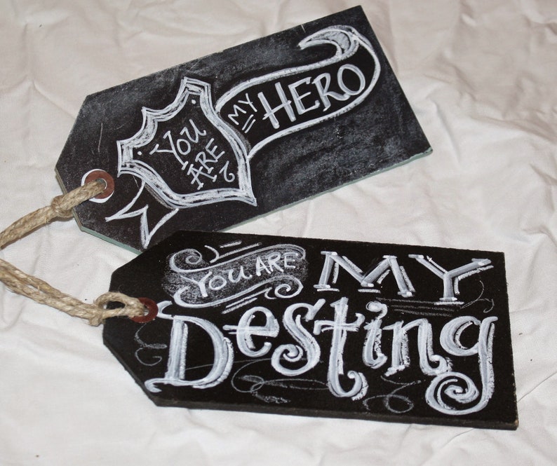 May include: Two black chalkboard tags with white chalk lettering. The top tag says "You are my hero" with a banner design. The bottom tag says "You are my destiny" with a decorative flourish.