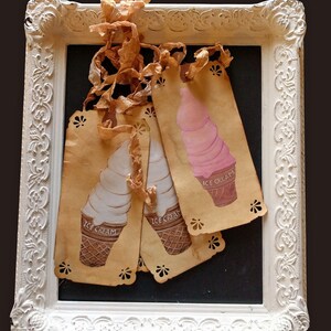 May include: Three vintage ice cream cone tags with a white frame. The tags are made of brown paper with a scalloped edge and feature illustrations of ice cream cones with the words "Ice Cream" printed on them.