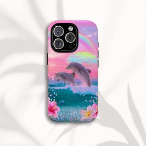 Puede incluir: Una funda de teléfono rosa con una vibrante ilustración de dos delfines saltando de olas turquesas bajo un arcoíris. El diseño incluye flores rosas y burbujas, sobre un cielo pastel.