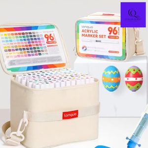 May include: A beige fabric carrying case with a set of 96 acrylic markers. The case is open, revealing the markers and a color chart. A second case is visible, along with two decorated Easter eggs. The brand name "Languo" is visible.