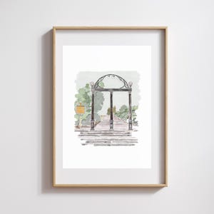 May include: Watercolor print of a black iron archway with three vertical supports, set against a backdrop of green foliage and a pathway. The artwork is framed in a light wood frame, showcasing a classic architectural design.