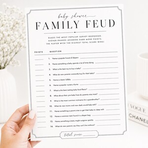 May include: A white paper game card for a baby shower titled Family Feud with black text. The card lists fourteen numbered questions about baby-related topics with blank lines for writing answers and a section at the bottom for total score.