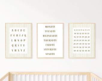 May include: Three framed prints with a neutral color palette. One print displays the alphabet, another lists the days of the week, and the third shows numbers 1-45. Each print has a white background with gold text and a gold striped border.