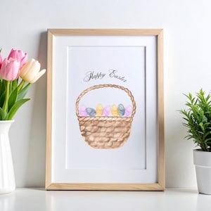 May include: Watercolor print of a basket filled with colorful Easter eggs. The basket has a woven design and a braided handle. The words "Happy Easter" are written above the basket in elegant script. The print is framed in a light wood frame.