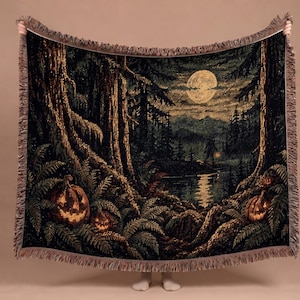 May include: A woven throw blanket featuring a dark forest scene at night with a full moon, tall trees, and ferns. The landscape includes glowing jack-o'-lanterns in the foreground and a silhouette of a creature standing near a reflective lake.