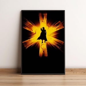May include: Framed art print featuring a silhouette of a person in a cape, set against a bright yellow and orange starburst design on a black background. The person is reaching out with one hand. The artwork is displayed on a wooden floor.