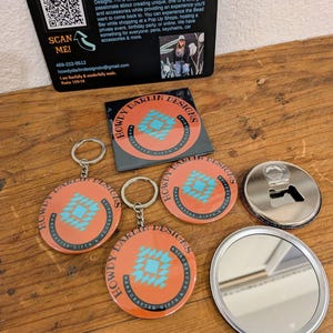 May include: A collection of Howdy Darlin' Designs accessories, including keychains, a bottle opener, and a compact mirror. The items feature an orange background with a turquoise geometric design and the brand's name. A business card is also present.
