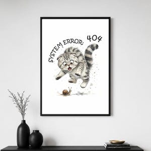 May include: A framed wall art print featuring a watercolour illustration of a surprised grey tabby kitten with folded ears jumping towards a small brown snail. The text "SYSTEM ERROR: 404" is printed in black above the kitten on a white background.