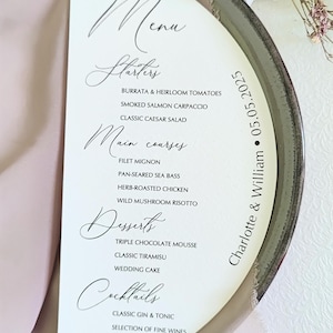 May include: A semi-circular white wedding menu card featuring black text that reads The Menu, Starters, Main courses, Desserts, Cocktails, and lists various food items. The right edge includes the text Charlotte & William and the date 05.05.2025.