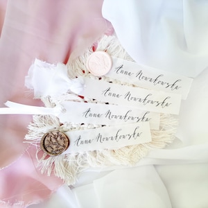 May include: Four white rectangular paper place cards with frayed edges, each featuring the name Anna Nowakowska in black calligraphy. One card has a pale pink wax seal, and another has a bronze-colored wax seal with a leaf pattern design.