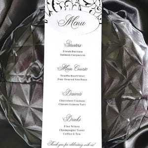 Peut inclure: Une carte de menu rectangulaire blanche avec des accents floraux noirs et un texte en écriture élégante. Le menu liste Starters, Main Course, Desserts et Drinks, incluant Fresh Burrata, Truffle Beef Fillet et Chocolate Fondant, se terminant par Thank you for celebrating with us.