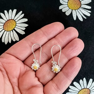May include: A pair of silver dangle earrings with a small daisy design. The center of the daisy is gold.