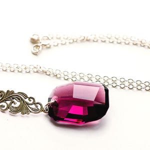 May include: A silver necklace with a large, faceted, magenta-colored pendant. The pendant is a deep, rich shade of pink. The necklace chain is delicate and the design includes an ornate silver accent piece.