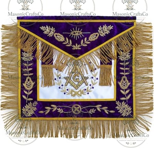 Puede incluir: Un delantal masónico morado y dorado con bordados intrincados. El delantal presenta un panel central blanco con símbolos masónicos, rodeado por un borde de terciopelo morado y flecos dorados. El texto "MasonicCraftsCo" es visible.