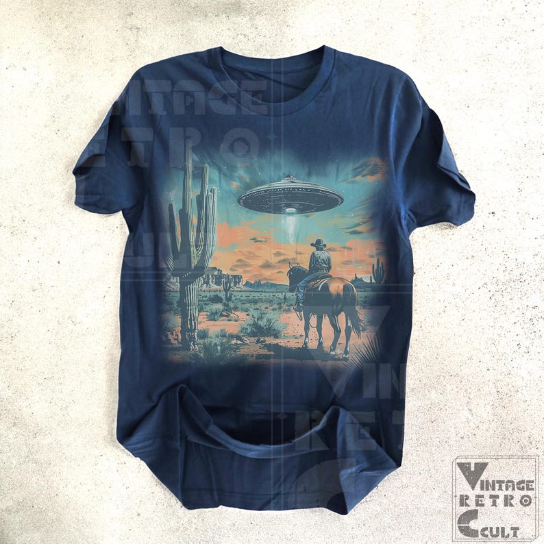 Pu&ograve; includere: Una t-shirt blu navy con una stampa grafica di un cowboy a cavallo in un paesaggio desertico con un UFO nel cielo. La grafica &egrave; sbiadita e ha un aspetto vintage.
