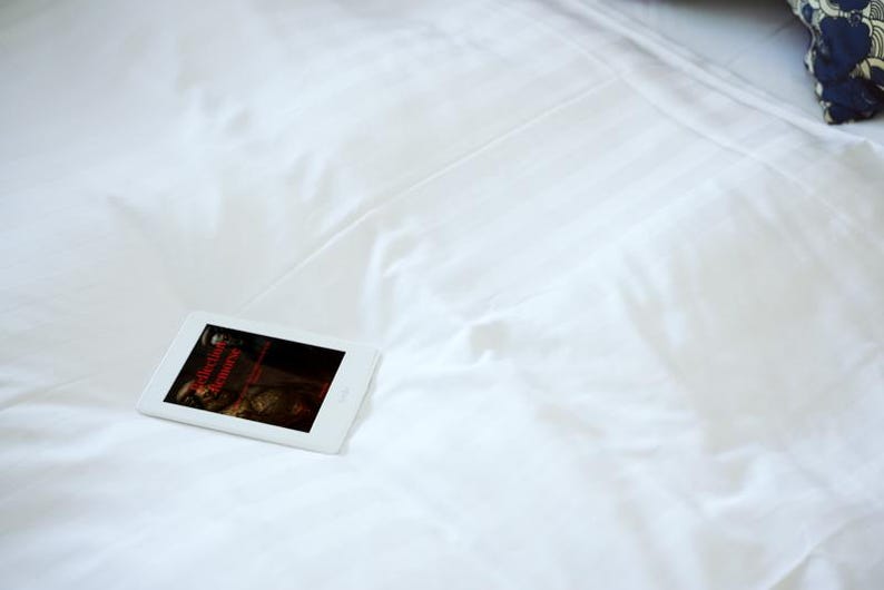 May include: A white tablet displaying a dark image with red text, resting on a white bedsheet. The bedsheet has subtle vertical lines. A patterned pillow is visible in the background.