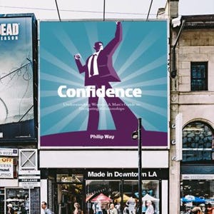 May include: A large billboard displays the word "Confidence" with a stylized illustration of a man in a suit. The billboard is above a storefront with the text "Made in Downtown LA". People are walking on the sidewalk.