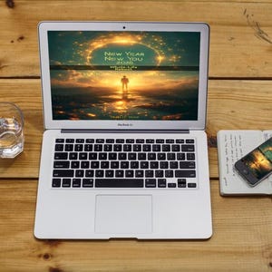 Może przedstawiać: Srebrny laptop wyświetla obraz zachodu słońca z tekstem "NEW YEAR NEW YOU 2020". Smartfon, notatnik i szklanka wody leżą na drewnianej powierzchni. Klawiatura laptopa jest czarna.