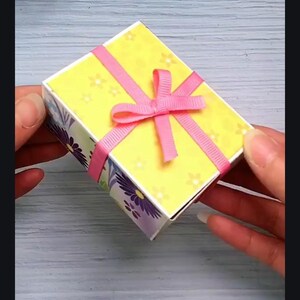 May include: A small yellow gift box with a pink ribbon and bow. The box has a floral pattern on the sides.