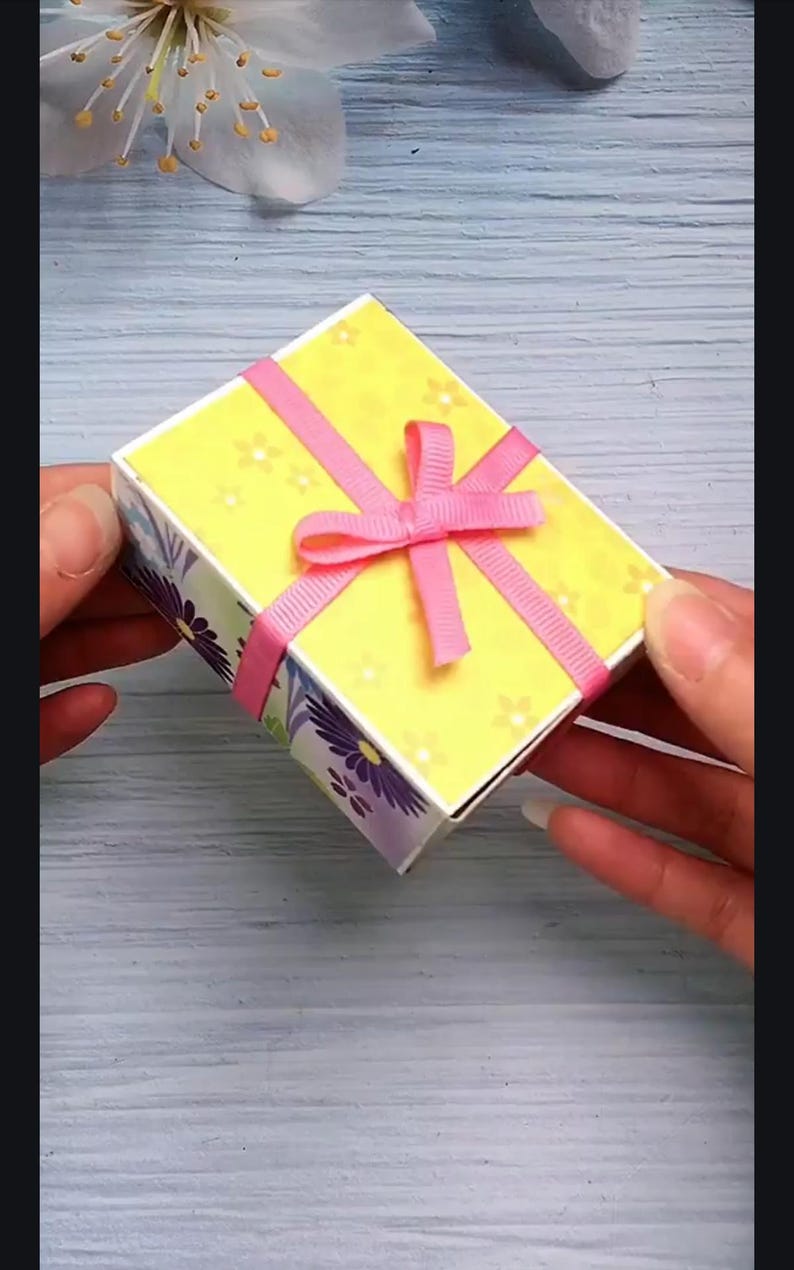May include: A small yellow gift box with a pink ribbon and bow. The box has a floral pattern on the sides.