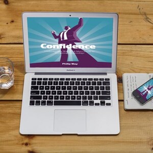 May include: A silver laptop displays the word "Confidence" with a graphic of a person. A smartphone and notebook are nearby. A glass of water sits to the left on a wooden surface.