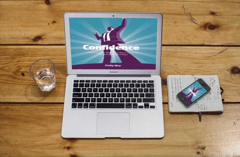 May include: A silver laptop displays the word "Confidence" with a graphic of a person. A smartphone and notebook are nearby. A glass of water sits to the left on a wooden surface.