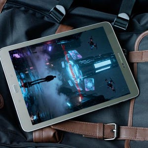 K&ouml;nnte beinhalten: Ein silbernes Samsung-Tablet, das eine futuristische Videospielszene mit einer Silhouette und fliegenden Drohnen zeigt. Das Tablet liegt auf einem schwarz-braunen Rucksack mit Lederriemen und Schnalle.