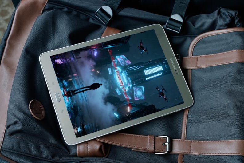 K&ouml;nnte beinhalten: Ein silbernes Samsung-Tablet, das eine futuristische Videospielszene mit einer Silhouette und fliegenden Drohnen zeigt. Das Tablet liegt auf einem schwarz-braunen Rucksack mit Lederriemen und Schnalle.