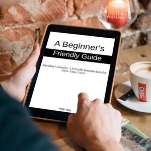 Op de afbeelding: Een tablet met de tekst "A Beginner's Friendly Guide" en de ondertitel "Smoking Cannabis: A Friendly Introduction for First-Time Users". Op de achtergrond een kopje koffie en een brandende kaars in een glazen houder, tegen een bakstenen muur.