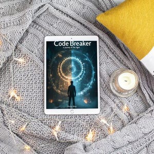 May include: A tablet displaying the book cover of "Code Breaker: A Journey of the Ages" rests on a gray knitted blanket. A yellow pillow, a candle in a glass holder, and a decorative pillow with blue accents are also present. String lights are draped across the blanket.