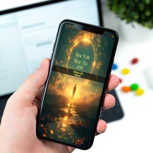 Może przedstawiać: Czarny smartfon wyświetla motywacyjny obraz z tekstem "New Year New You 2026" i "Whole-Life Reboot". Ekran pokazuje osobę na ścieżce do jasnego światła, z złotym, świecącym tłem. Telefon jest trzymany w dłoni.