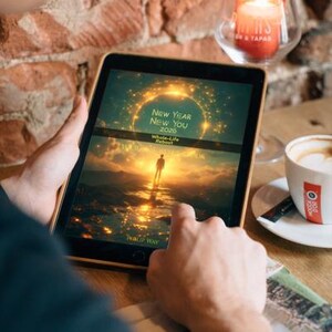 Może przedstawiać: Osoba trzymająca tablet z tekstem "New Year New You 2020 Whole-Life Reboot" ze zdjęciem zachodu słońca. Na stole zapalona świeca i filiżanka kawy. Tło to ceglana ściana.