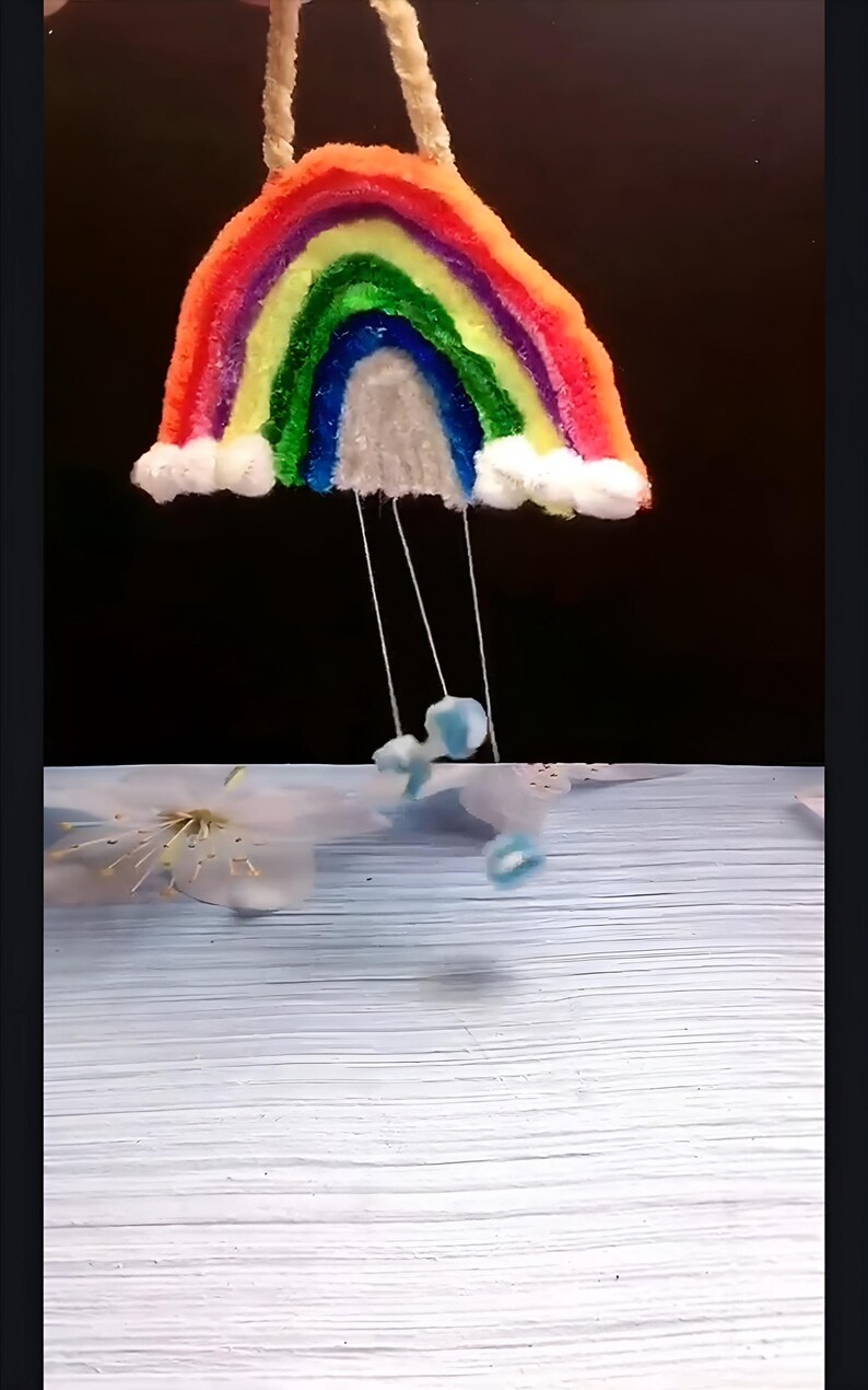 May include: A rainbow-colored yarn craft hanging from the ceiling with white cotton clouds and blue yarn raindrops hanging below.