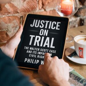 May include: A tablet displaying the book cover of "Justice on Trial" by Philip W. The cover features white text on a black background. A cup of coffee and a lit candle are also visible in the image.