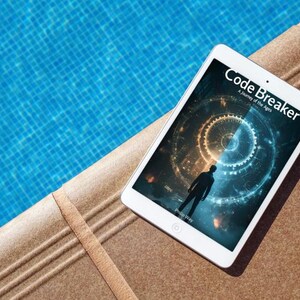 May include: A white tablet displaying the book cover of "Code Breaker: A Journey of the Ages" with a silhouette of a person. The tablet rests on a brown surface next to a blue pool.