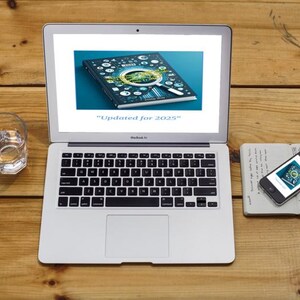 Puede incluir: Un port&aacute;til que muestra un gr&aacute;fico digital con una lupa, un tel&eacute;fono inteligente, un cuaderno y un vaso de agua sobre una superficie de madera. La pantalla del port&aacute;til dice "Actualizado para 2025".