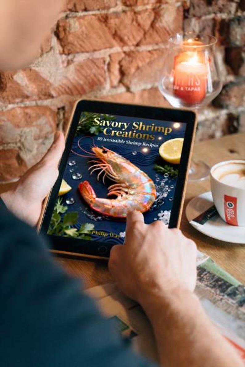 May include: A person holding a tablet displaying the cover of "Savory Shrimp Creations: 50 Irresistible Shrimp Recipes." The cover features a large shrimp, lemon slices, and parsley on a dark blue background. A lit candle and a cup of coffee are also visible.