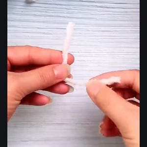 May include: A person's hands are shown holding two white pipe cleaners, twisting them together.