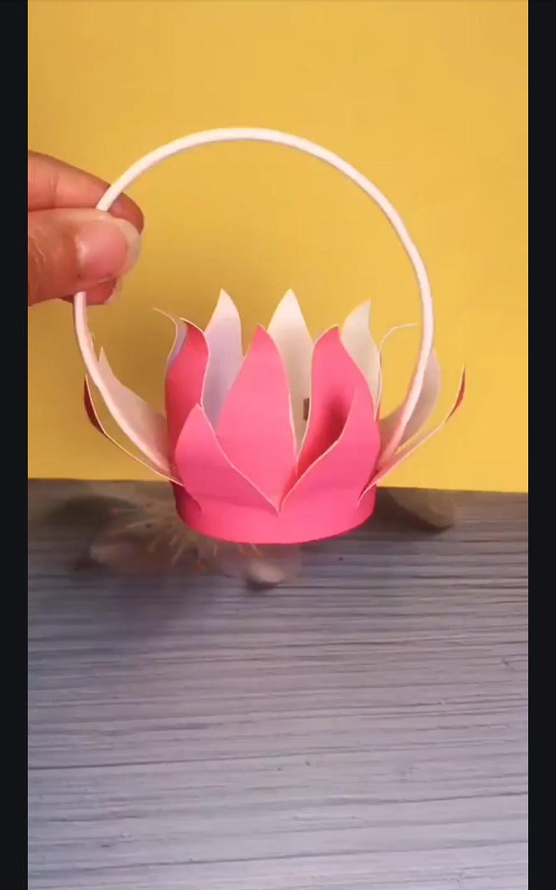 May include: A pink and white paper flower with a white paper handle. The flower is shaped like a lotus.