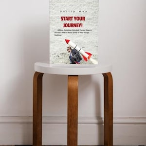 May include: A book titled "Start Your Journey!" with a rocket illustration, resting on a small, round, white table with wooden legs. The book cover features text and an image of a person with a rocket.